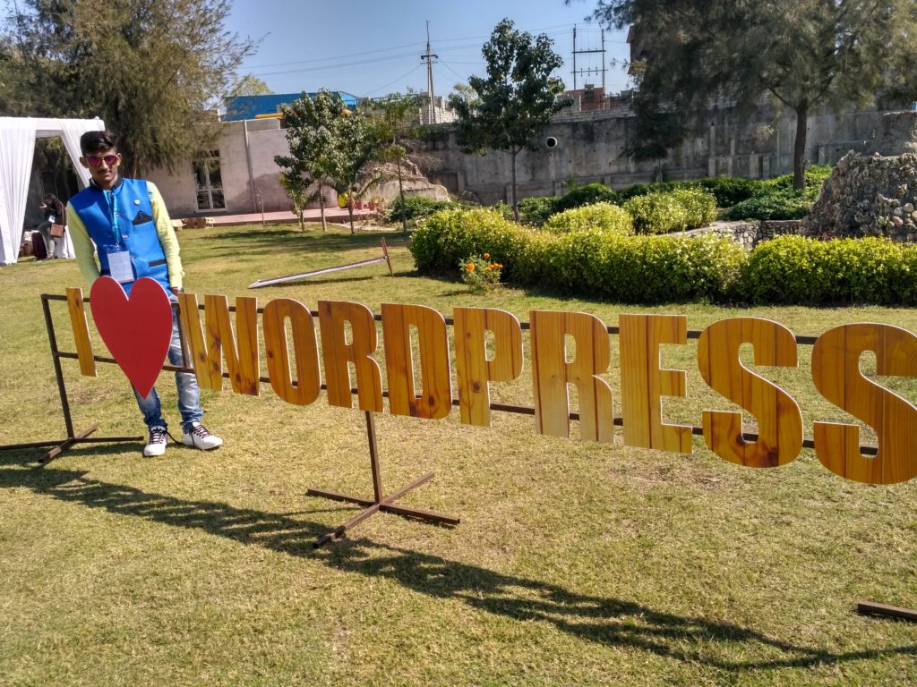 Pravin standing by a long sign that says I Heart WordPress