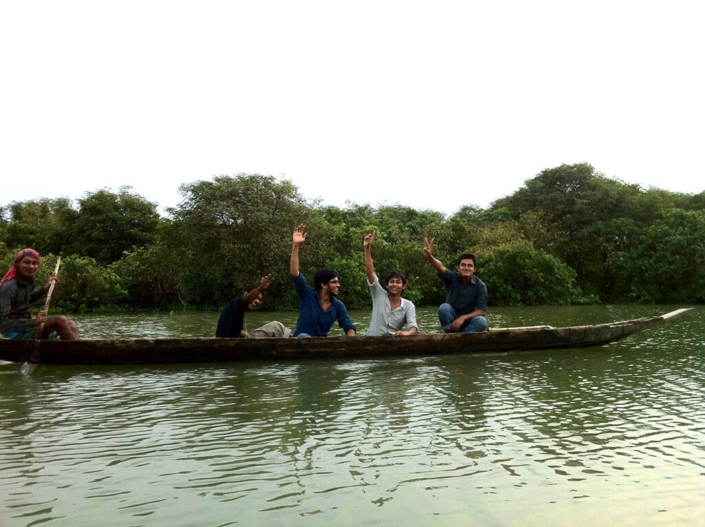 Four young men in a canoe, waving at the camera