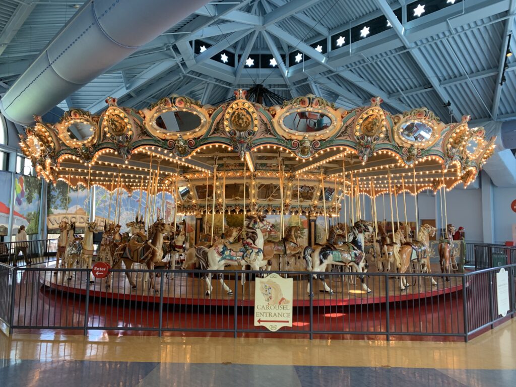 A traditional vacant carousel with ornately decorated horses and a lit canopy with a sign indicating the entrance at the Please Touch Museum (Philadelphia, Pennsylvania)