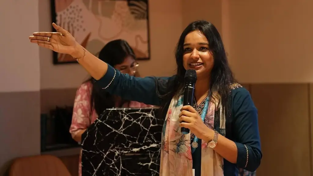 Astha holding a microphone and gesturing with one hand.